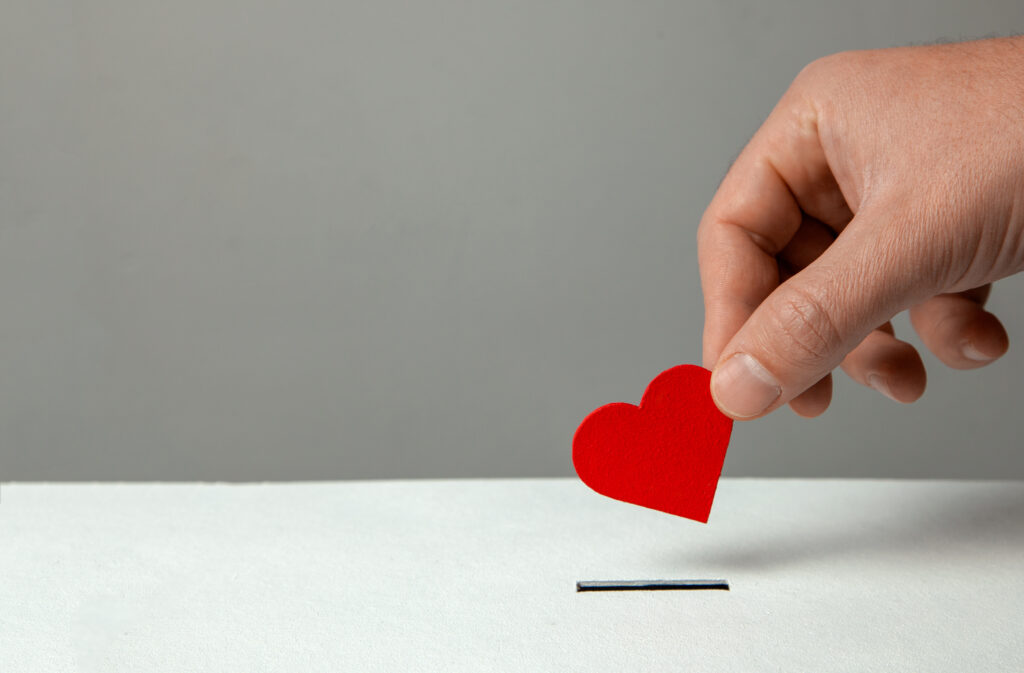 Man’s hand places heart in the donation slot.